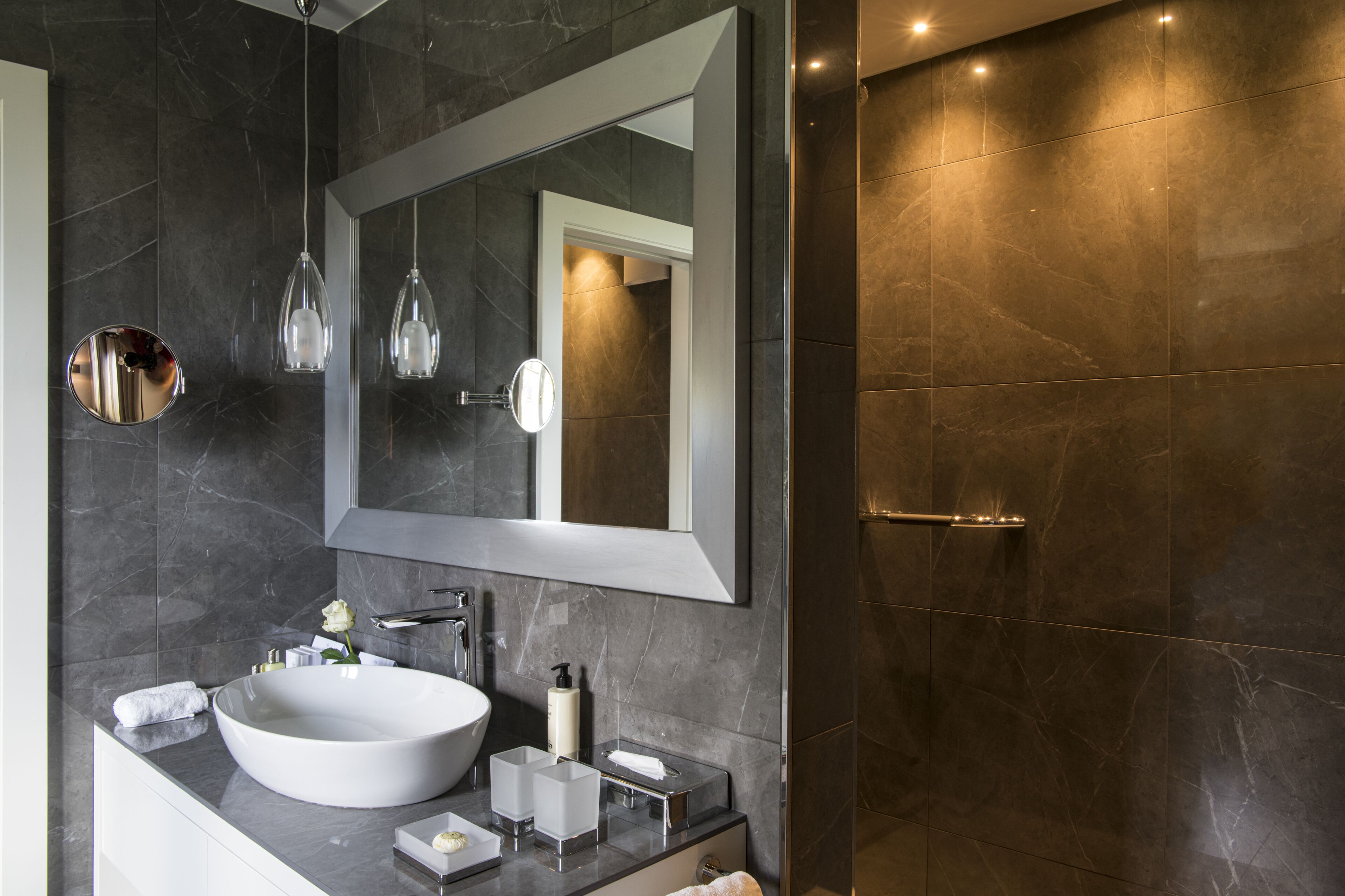 Un baño moderno con un lavamanos grande de color blanco, un espejo y luces colgantes.