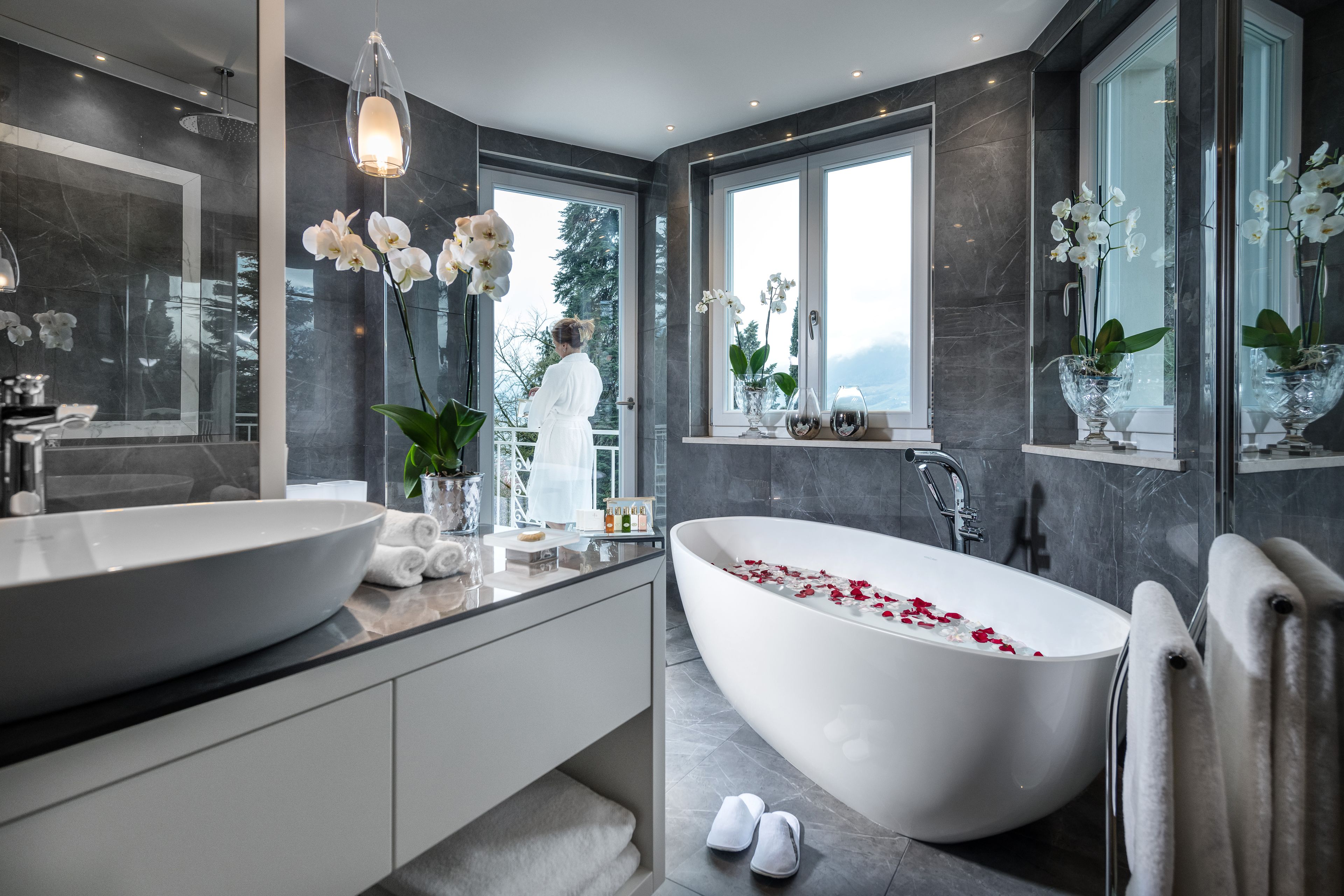 A modern bathroom with a large freestanding bathtub, a double sink vanity, and large windows offering a view of the outdoors.
