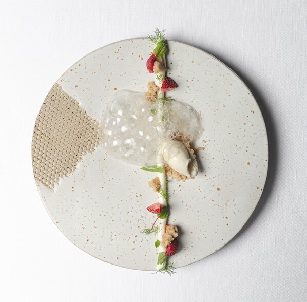 A round plate with a dessert featuring a honeycomb-like structure, a scoop of ice cream, and garnishes of strawberries and herbs. - VILLA EDEN - The Private Retreat (Merano)