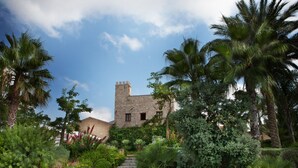 Un bâtiment historique en pierre, doté d’une tour, entouré d’une végétation luxuriante et de palmiers.