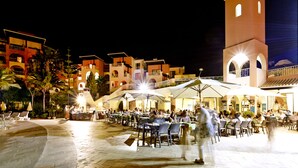 An outdoor dining area with tables and chairs, a tower, and buildings in the background. - Four Seasons Vilamoura (Loulé)