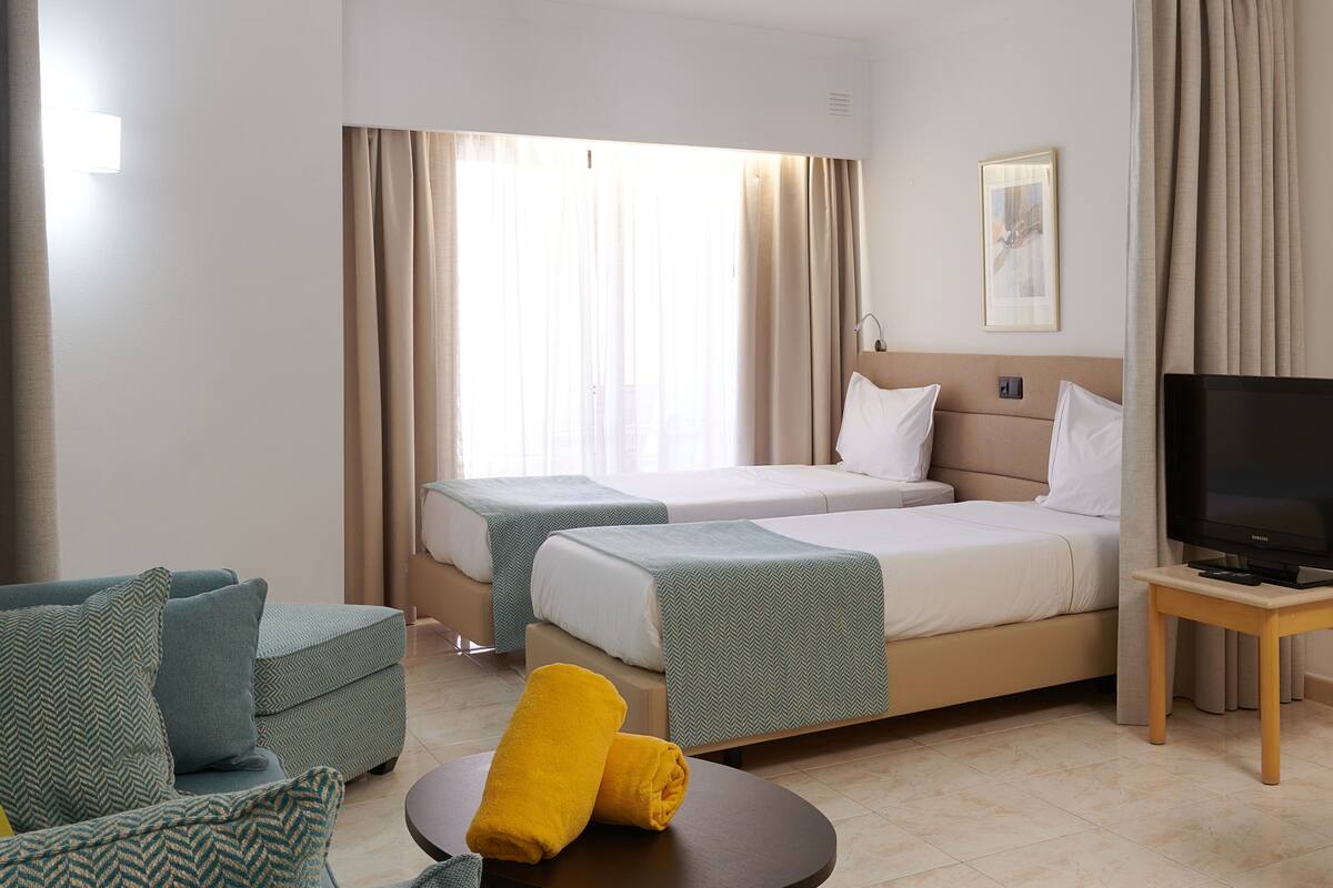A hotel room with two beds, a sofa, a TV, and a window with curtains.