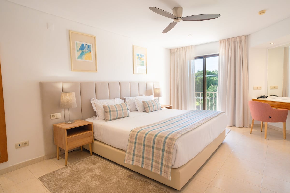 A bedroom with a bed, bedside tables, a desk, and a ceiling fan.