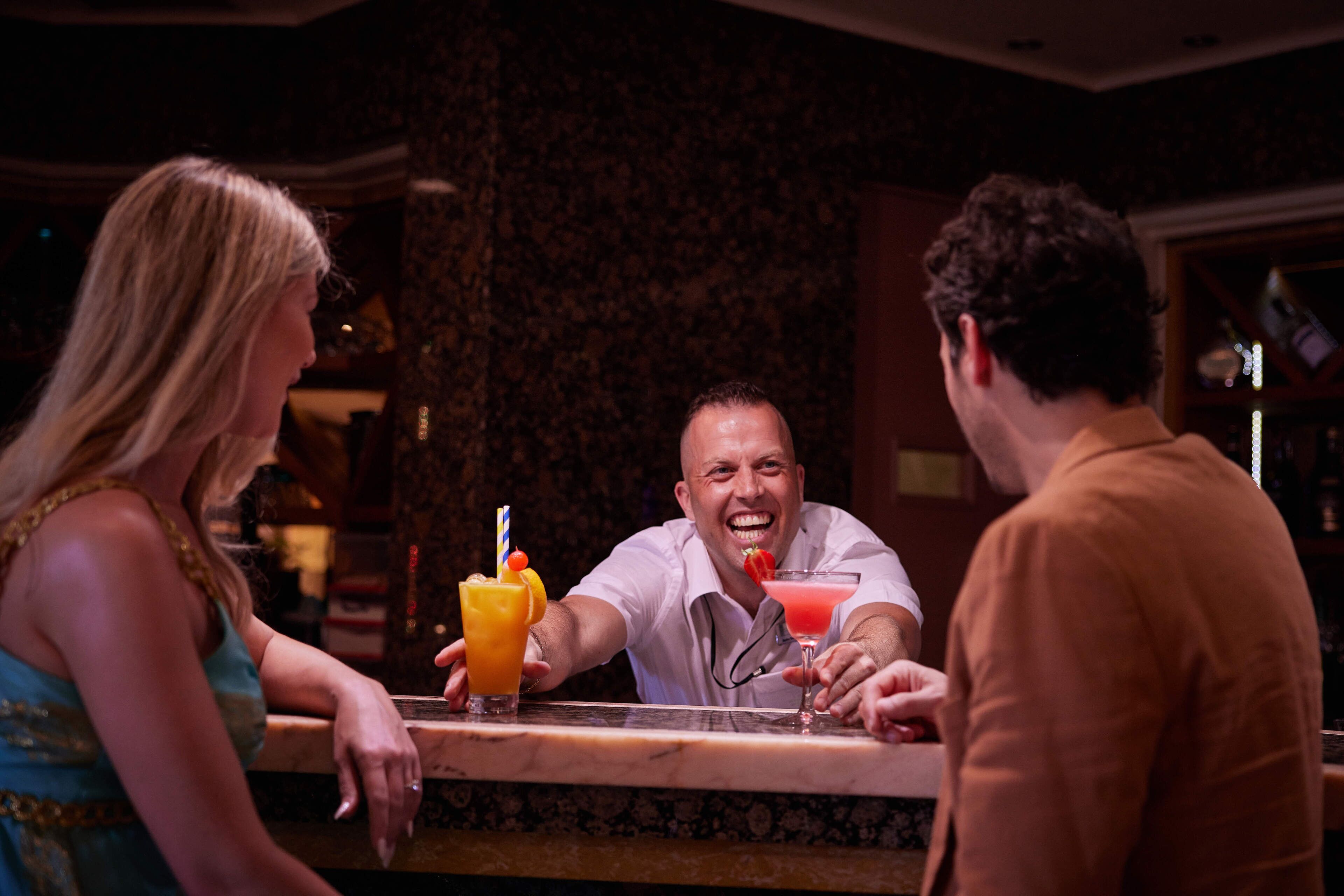 A bar area with a marble countertop, two drinks, and a person serving.