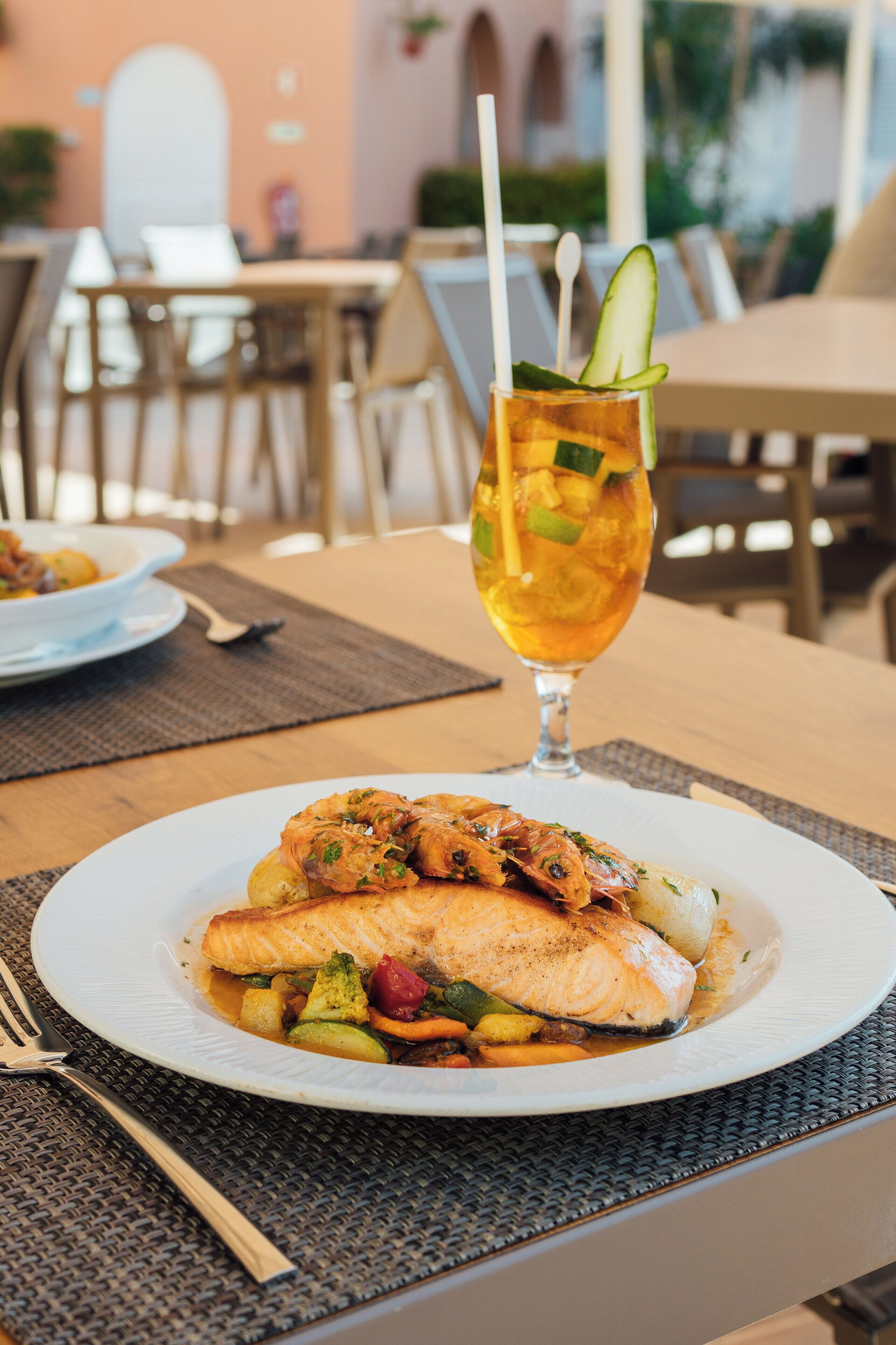Une table à manger avec une assiette de nourriture, un verre de thé glacé avec une paille et une fourchette.