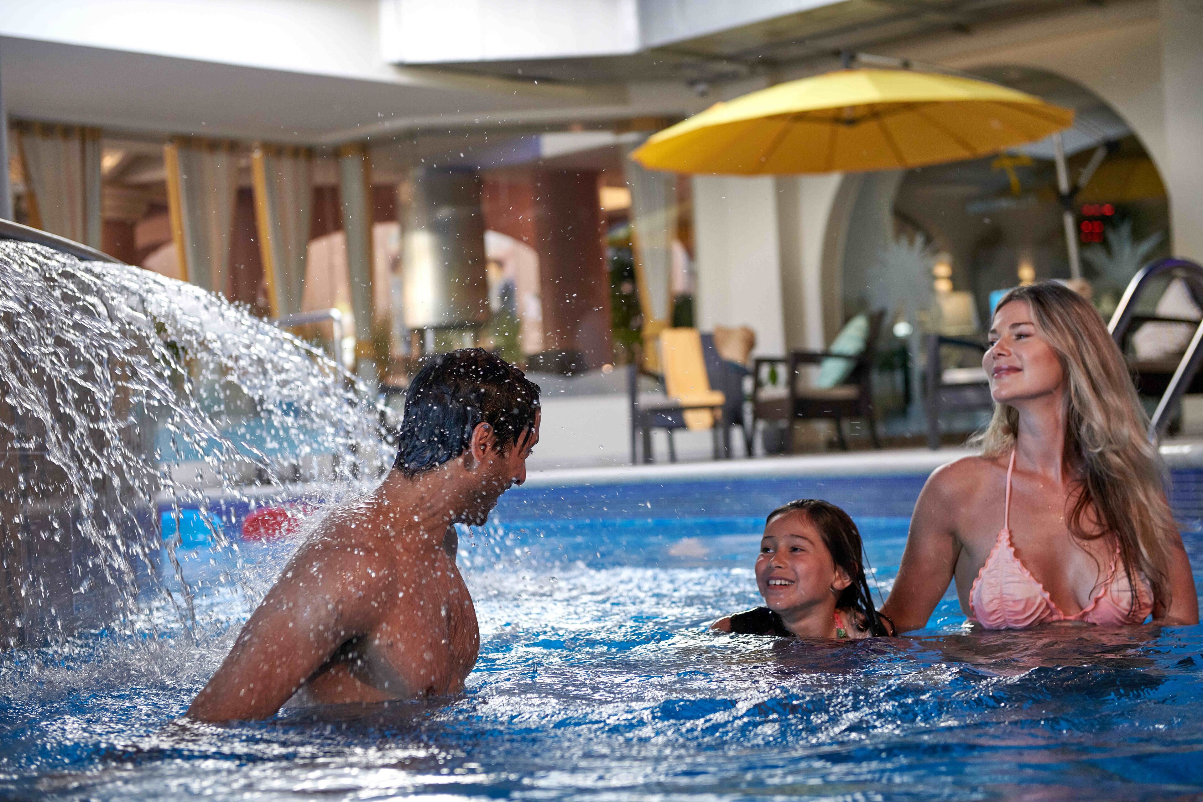 A pool area with a water feature, a yellow umbrella, and a seating area in the background.