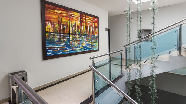A modern interior with a large abstract painting on the wall, a glass railing, and a staircase with hanging plants. - Hotel Central Plaza Medellin (Itagüí)