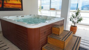 A hot tub with wooden steps leading up to it, a potted plant, and a view of the sky through large windows. - Hotel Central Plaza Medellin (Itagüí)
