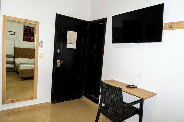 A room with a bed, a desk, a chair, a TV, and a door. - Hotel Central Plaza Medellin (Itagüí)