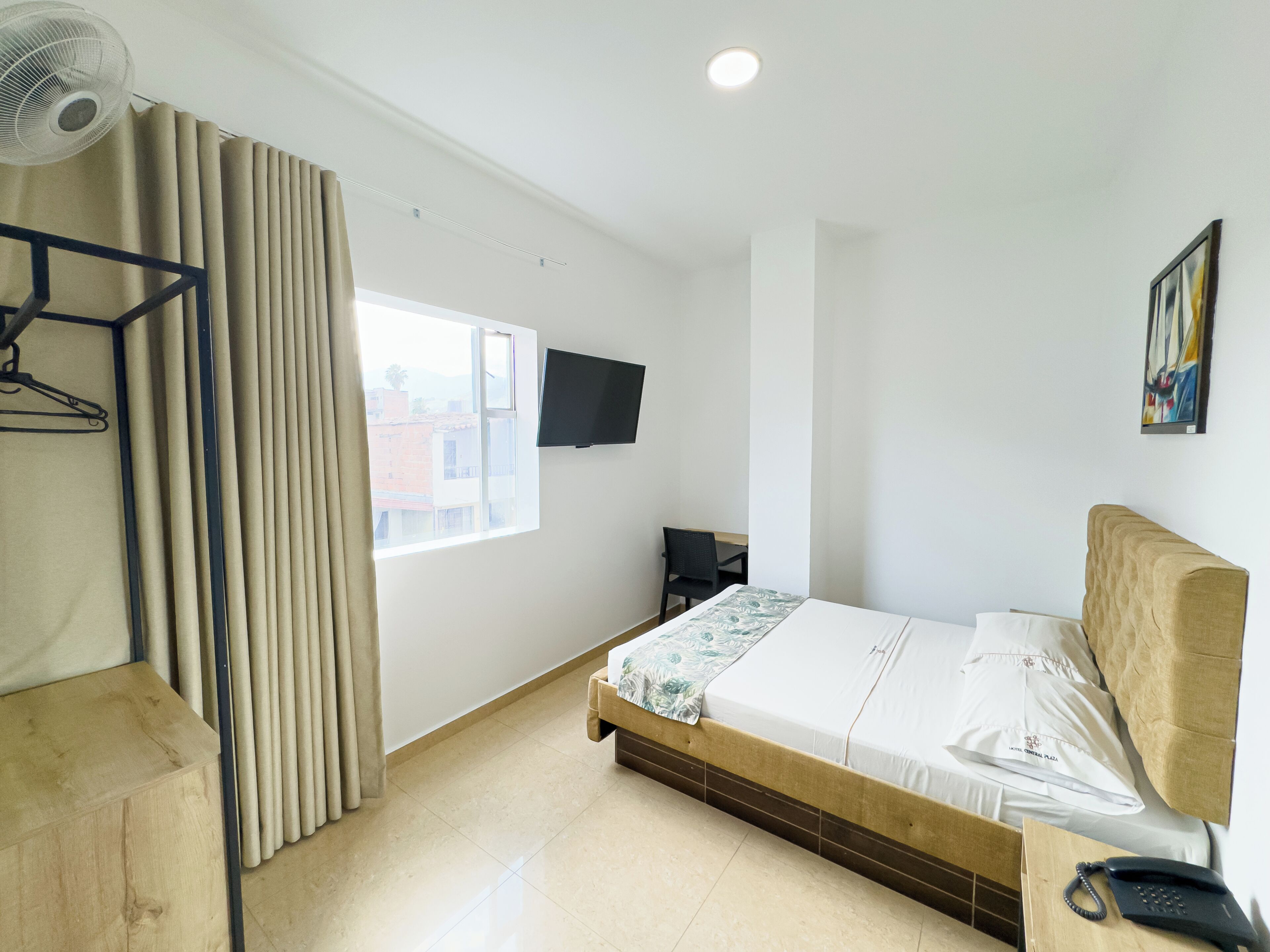 A hotel room with a bed, a desk, a chair, a TV, and a window with curtains.