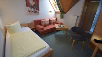 A room with a bed, a sofa, a small table, a chair, and a radiator.