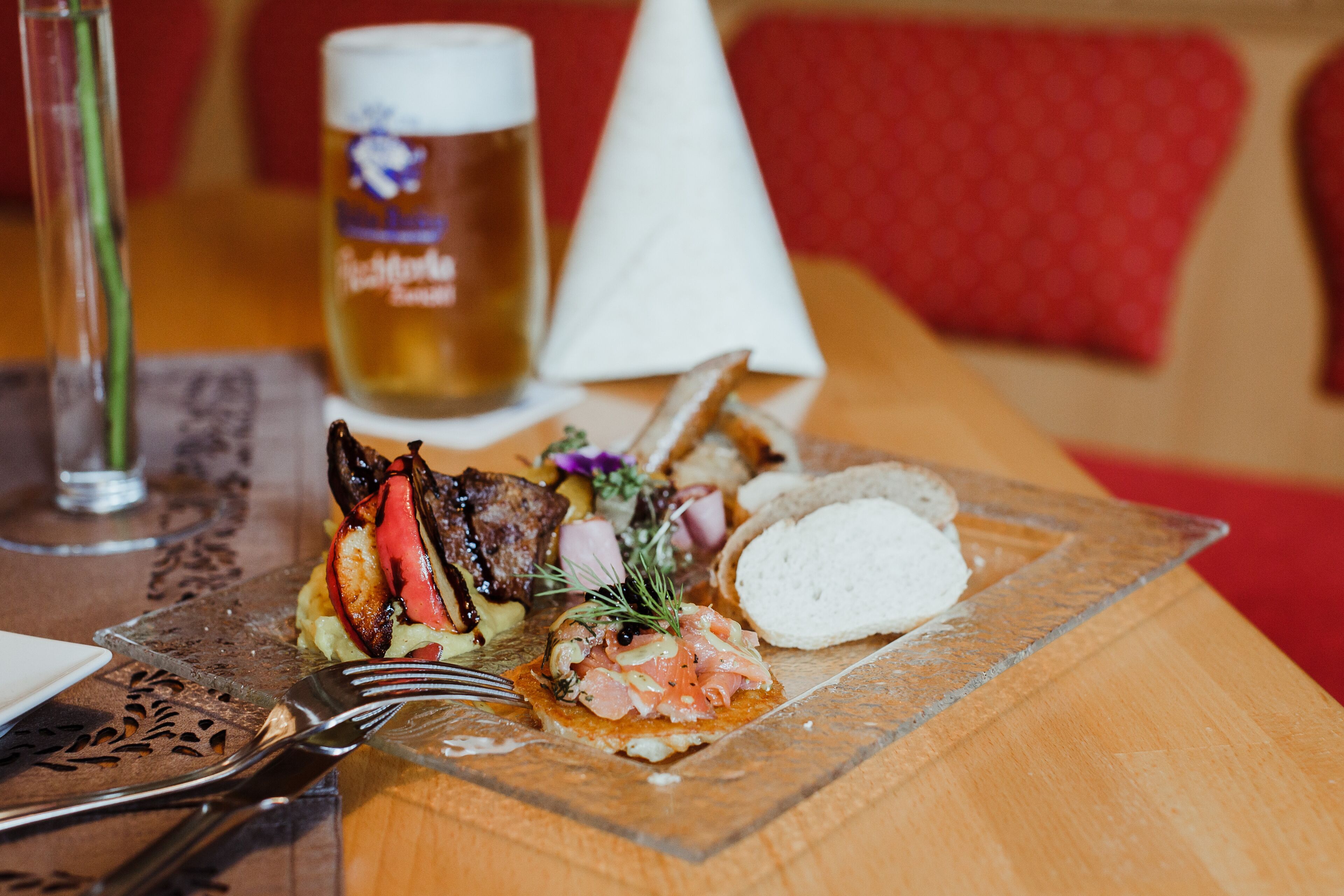 Una comida con varios platos, incluyendo un bistec, pan y una cerveza en una mesa de madera.