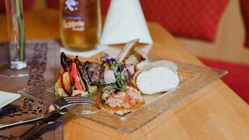Una comida con varios platos, incluyendo un bistec, pan y una cerveza en una mesa de madera.