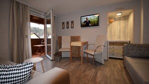 Ett modernt vardagsrum med en soffa, fåtöljer, ett litet bord, en tv som är monterad på väggen och en skjutdörr i glas som leder ut till ett utomhusområde.