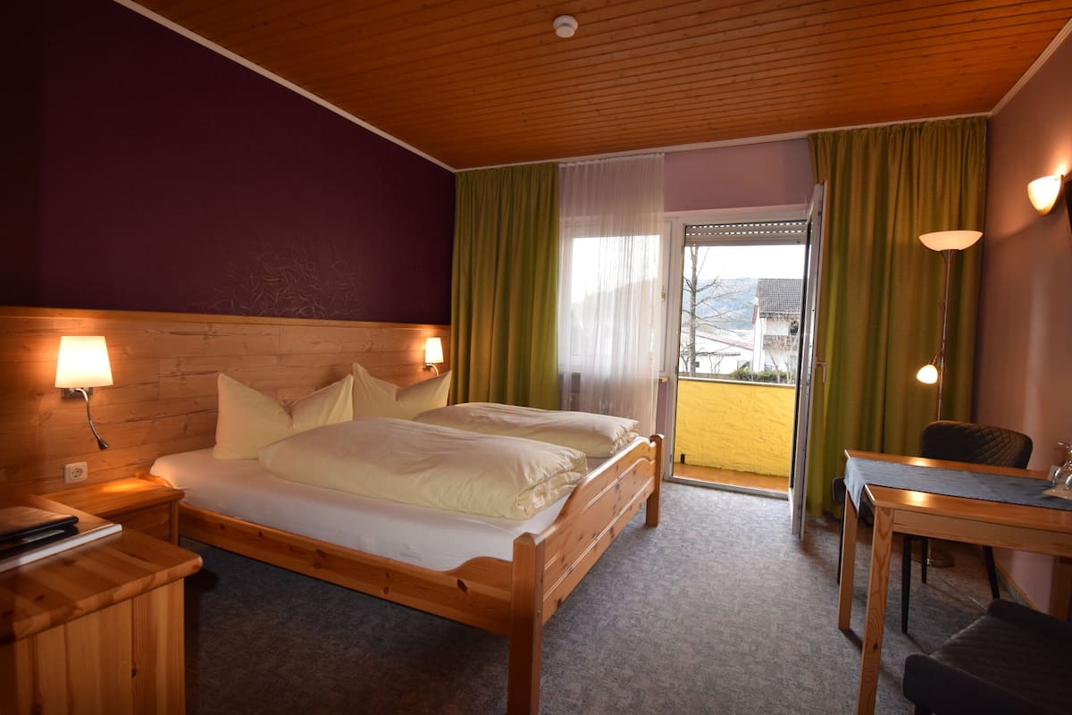 Een hotelkamer met een houten bed, twee bedlampen, een bureau en uitzicht op het omliggende gebied.