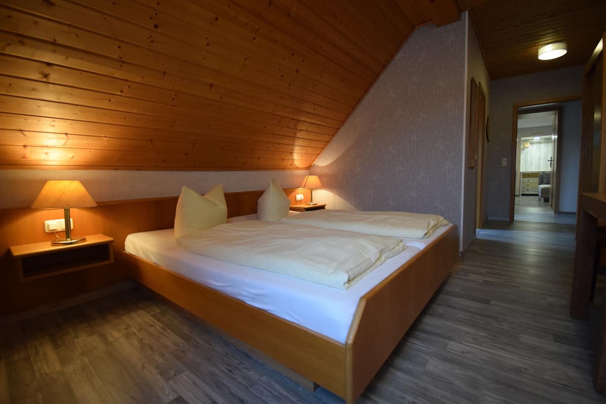 Een slaapkamer met een houten plafond, een bed met witte lakens, twee bedlampen en een nachtkastje.