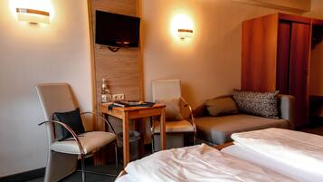 A hotel room with two single beds, a wooden desk with a chair, a television mounted on the wall, and two wall-mounted light fixtures.
