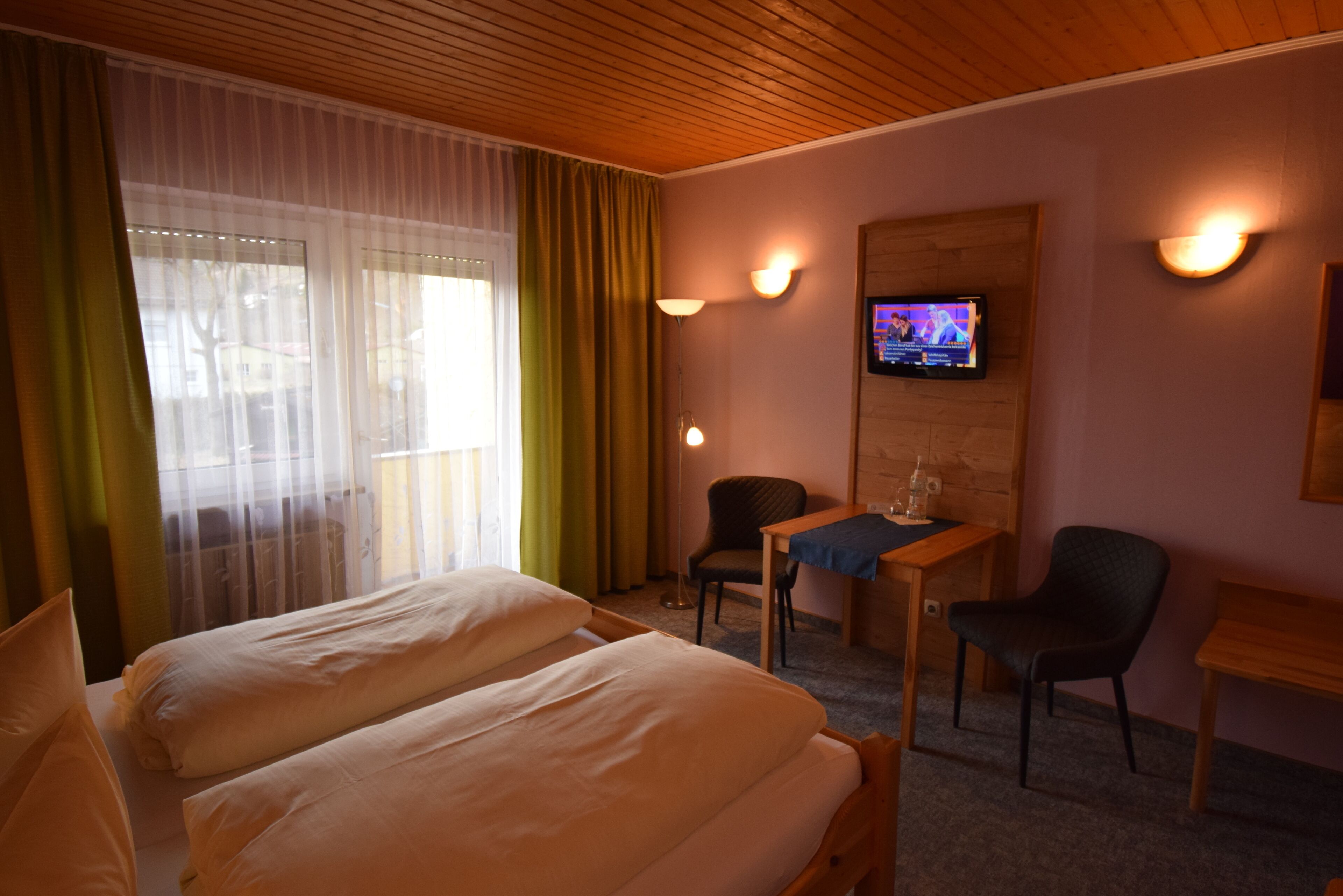 Une chambre d’hôtel avec deux lits, un bureau, une chaise, une télévision et une fenêtre avec des rideaux.