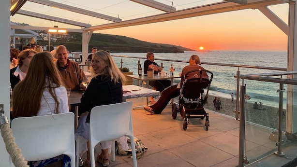 A sunset view from a covered outdoor seating area with tables and chairs, overlooking the sea. - The Nook (St Ives)