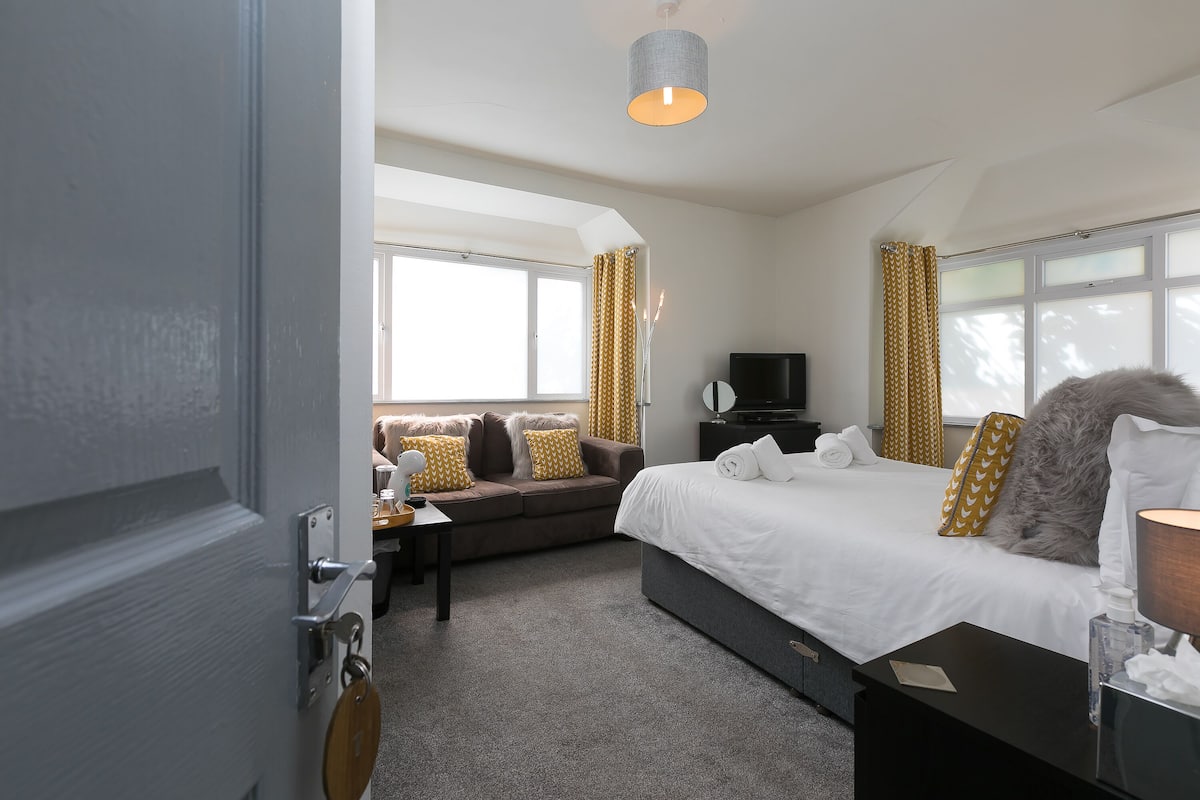 A hotel room with a bed, a sofa, a TV, and a desk with a lamp.