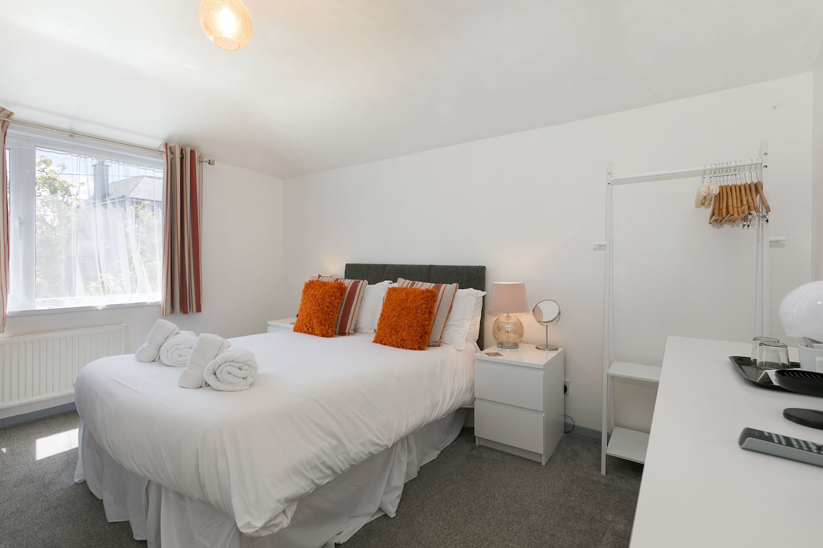 A neatly arranged hotel room with a bed, bedside tables, a desk, and a window with curtains.