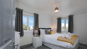 A bedroom with a bed, bedside tables, a lamp, and curtains. - The Nook (St Ives)