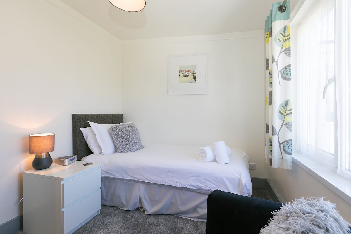 A neatly arranged bedroom with a bed, bedside table, lamp, and a window with curtains.
