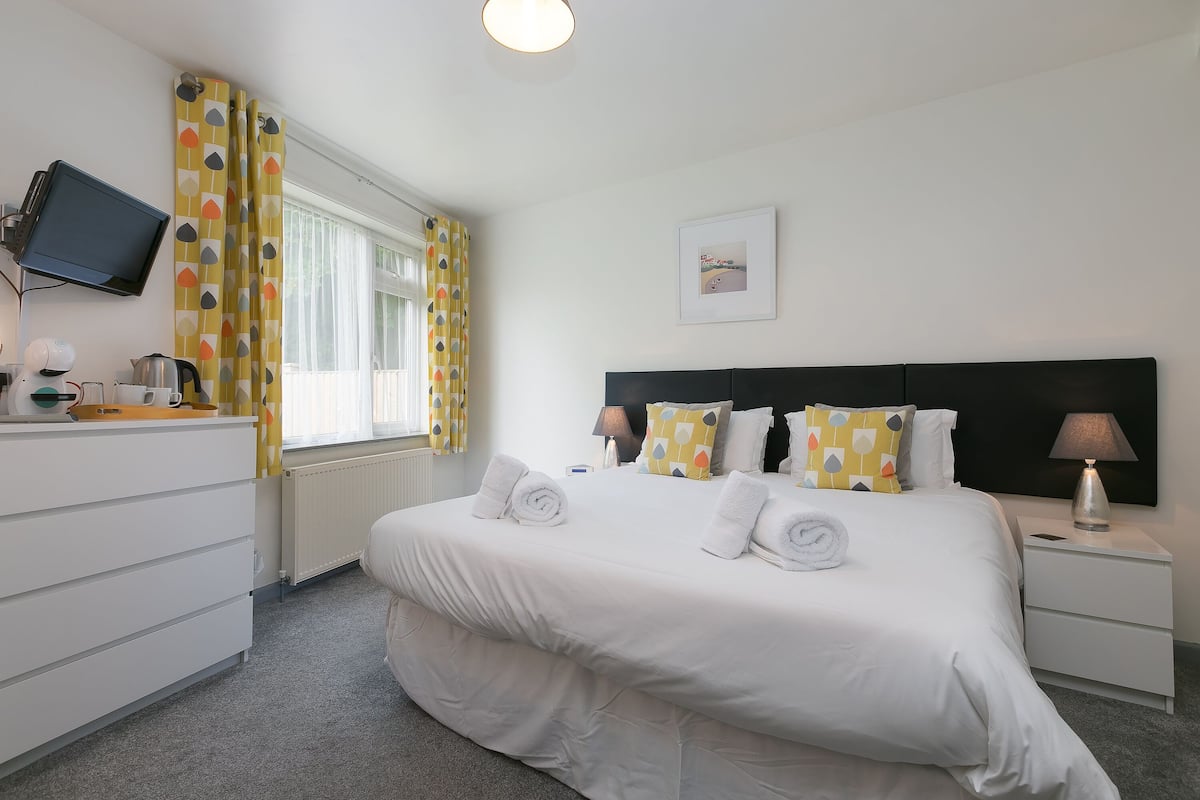A neatly arranged hotel room with a bed, a bedside table, a TV mounted on the wall, and a window with curtains.