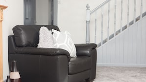 A black leather sofa with a white pillow and a small table with candles. - The Nook (St Ives)