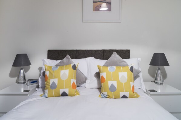 A neatly made bed with two pillows featuring a geometric pattern, flanked by two bedside tables with lamps and a small clock.
