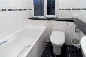 A modern bathroom with a bathtub, toilet, and a window. - The Nook (St Ives)