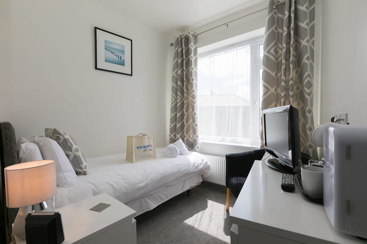 A hotel room with a bed, a desk with a computer, a TV, a lamp, and a bag on the bed.