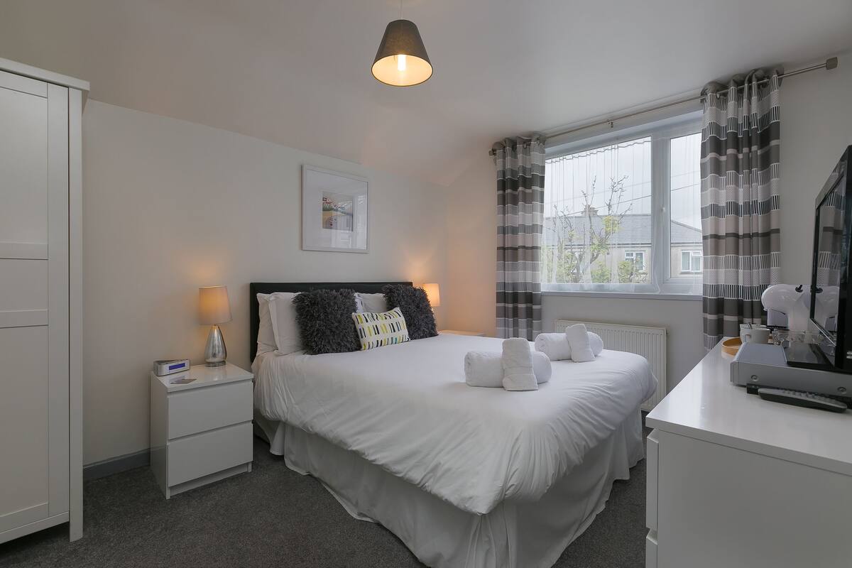 A neatly arranged bedroom with a bed, bedside table, lamp, and a window with curtains.