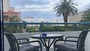 A balcony with a round table and two chairs, a palm tree, and buildings in the background. - Blue Roses (Rhodes)