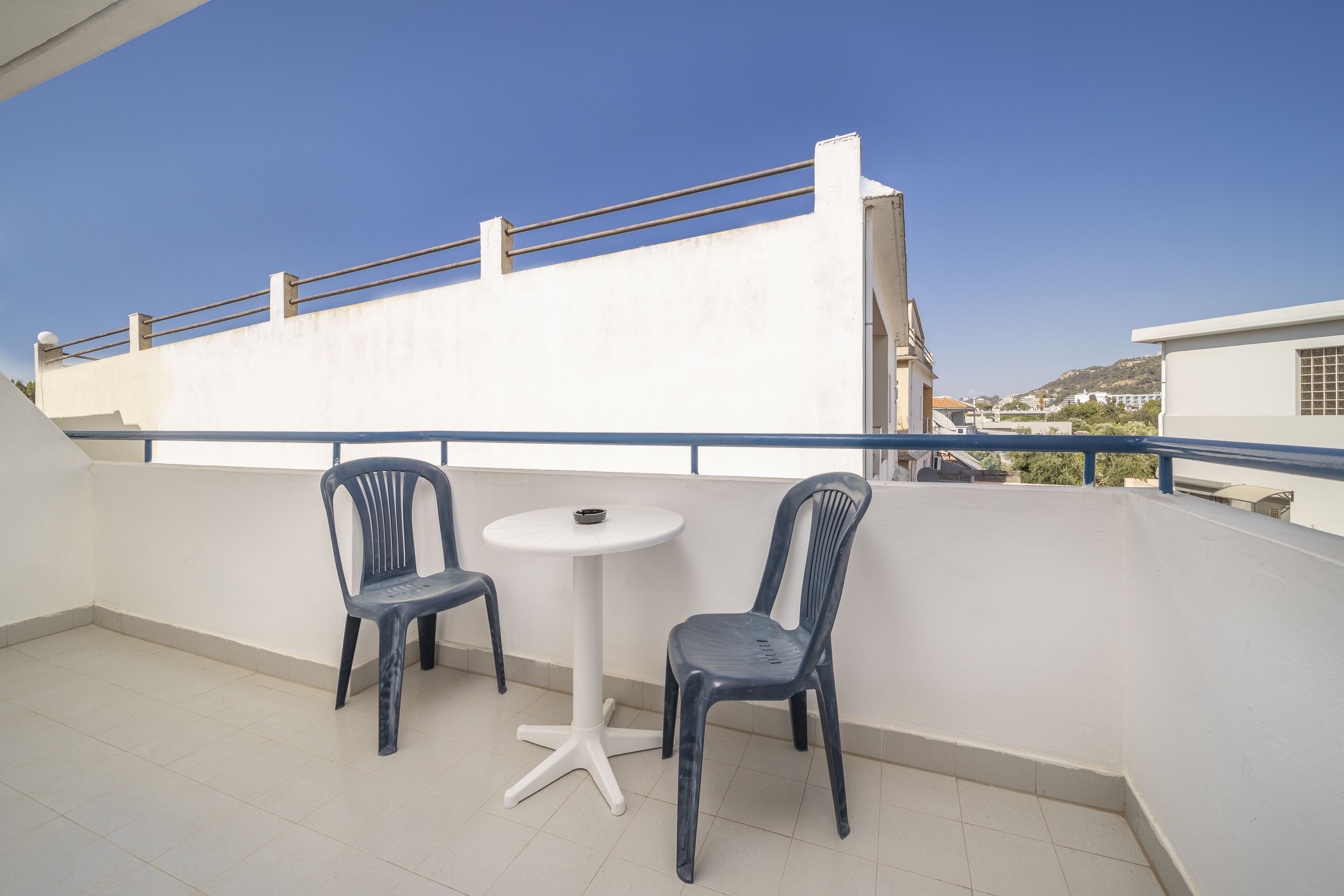 A balcony with two chairs and a small table, overlooking a cityscape.