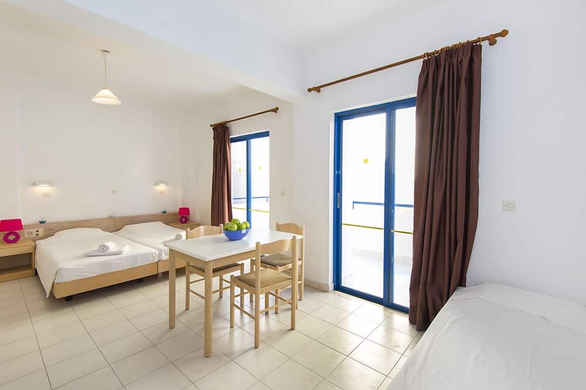 Habitación de hotel con dos camas, una mesa de comedor, sillas, un frutero y vistas a través de un ventanal grande.