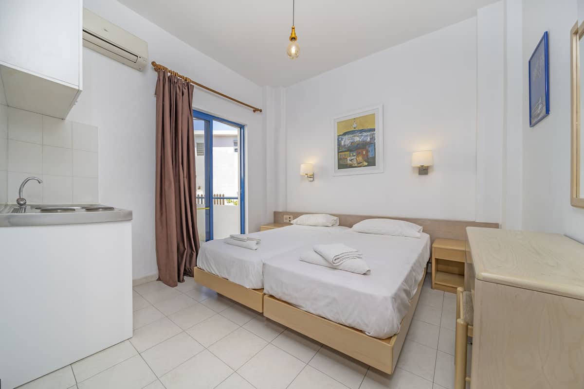 Habitación de hotel con kitchenette, dos camas, baño y balcón con vistas.