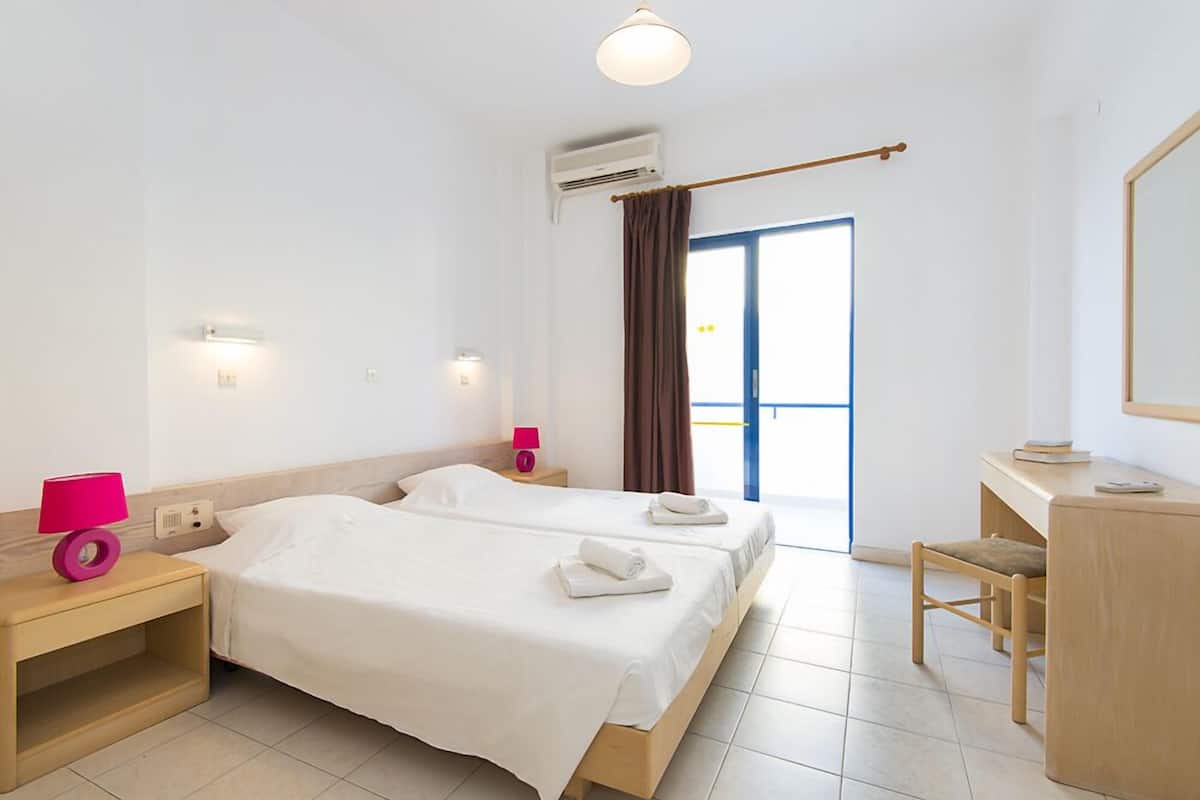Habitación de hotel con dos camas, un escritorio, una silla, un espejo y una ventana con cortinas.