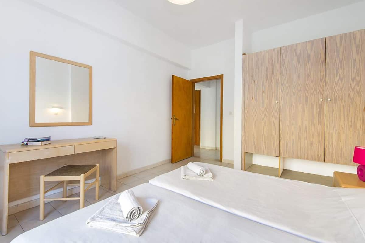 Habitación de hotel con dos camas, un escritorio, una silla, un armario y un espejo.