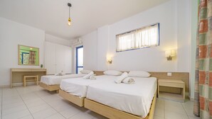A hotel room with two single beds, a desk, a chair, a small table, a wall-mounted shelf, and a window with curtains. - Blue Roses (Rhodes)
