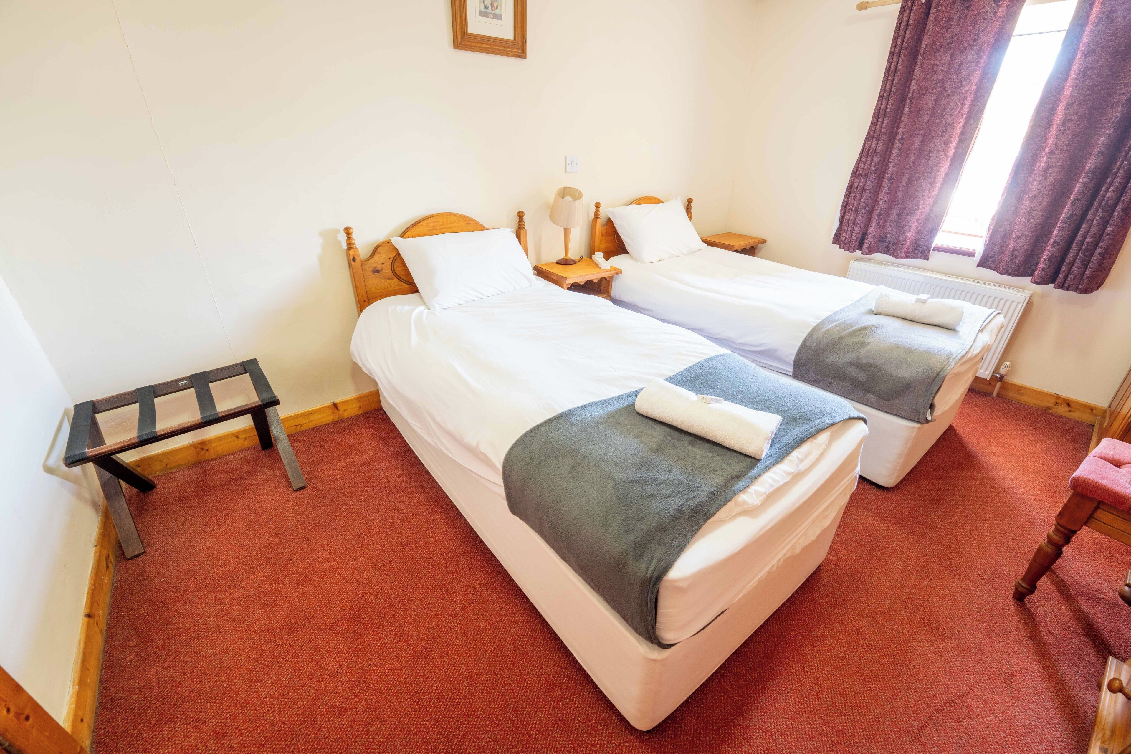 A room with two beds, a small table, a chair, and a window with curtains.