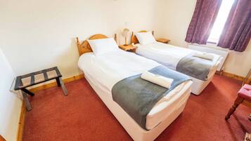 A room with two beds, a small table, a chair, and a window with curtains.