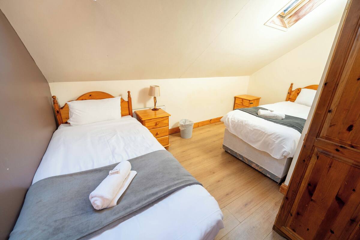 Une chambre avec deux lits, des têtes de lit en bois, une petite table de chevet avec une lampe et une poubelle.