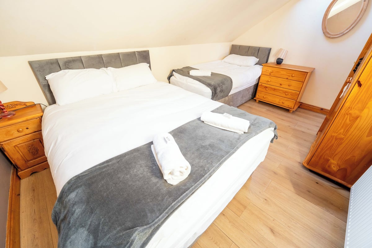 Une chambre avec deux lits, des tables de chevet en bois, une commode et un miroir.
