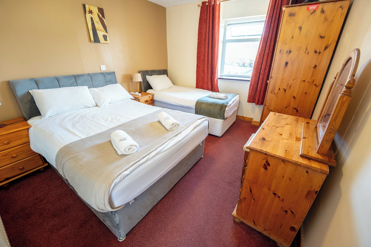 Une chambre d’hôtel avec deux lits, une commode en bois, un miroir et une fenêtre avec des rideaux.