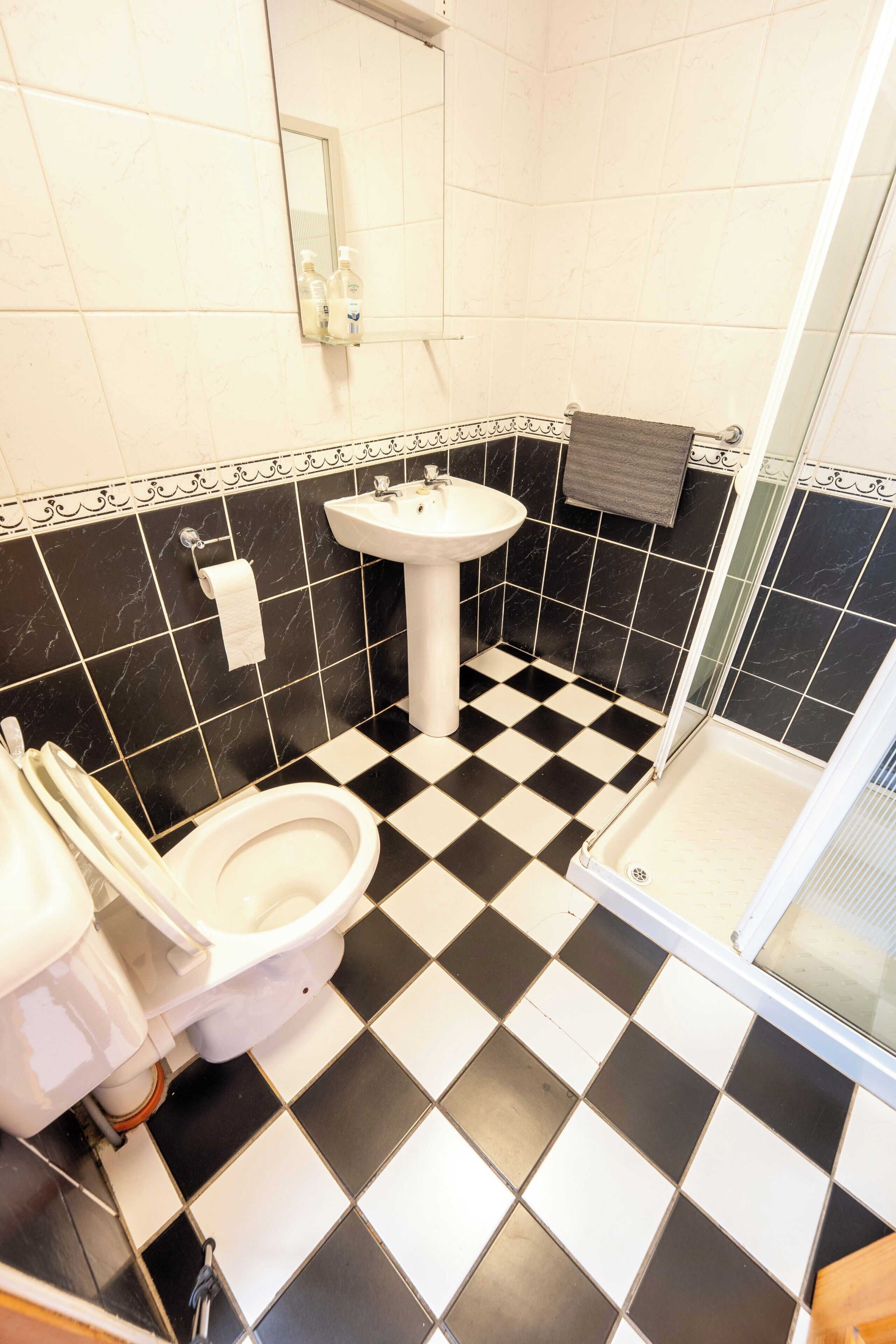 Une salle de bain avec un carrelage noir et blanc à motifs de damier, un lavabo blanc et des toilettes.