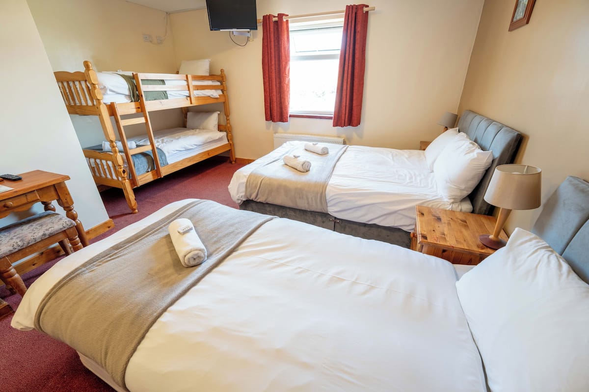 Une chambre avec deux lits simples, un lit superposé, un bureau, une chaise, une lampe et un téléviseur.