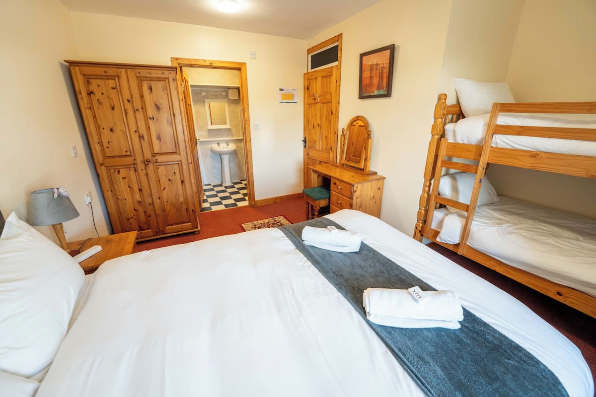 Une chambre d’hôtel avec un grand lit, un bureau, un miroir, une armoire et un lit superposé.