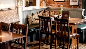 A cozy dining area with wooden furniture, a bench, and a brick wall with framed pictures. - Marquis Of Granby (Dover)