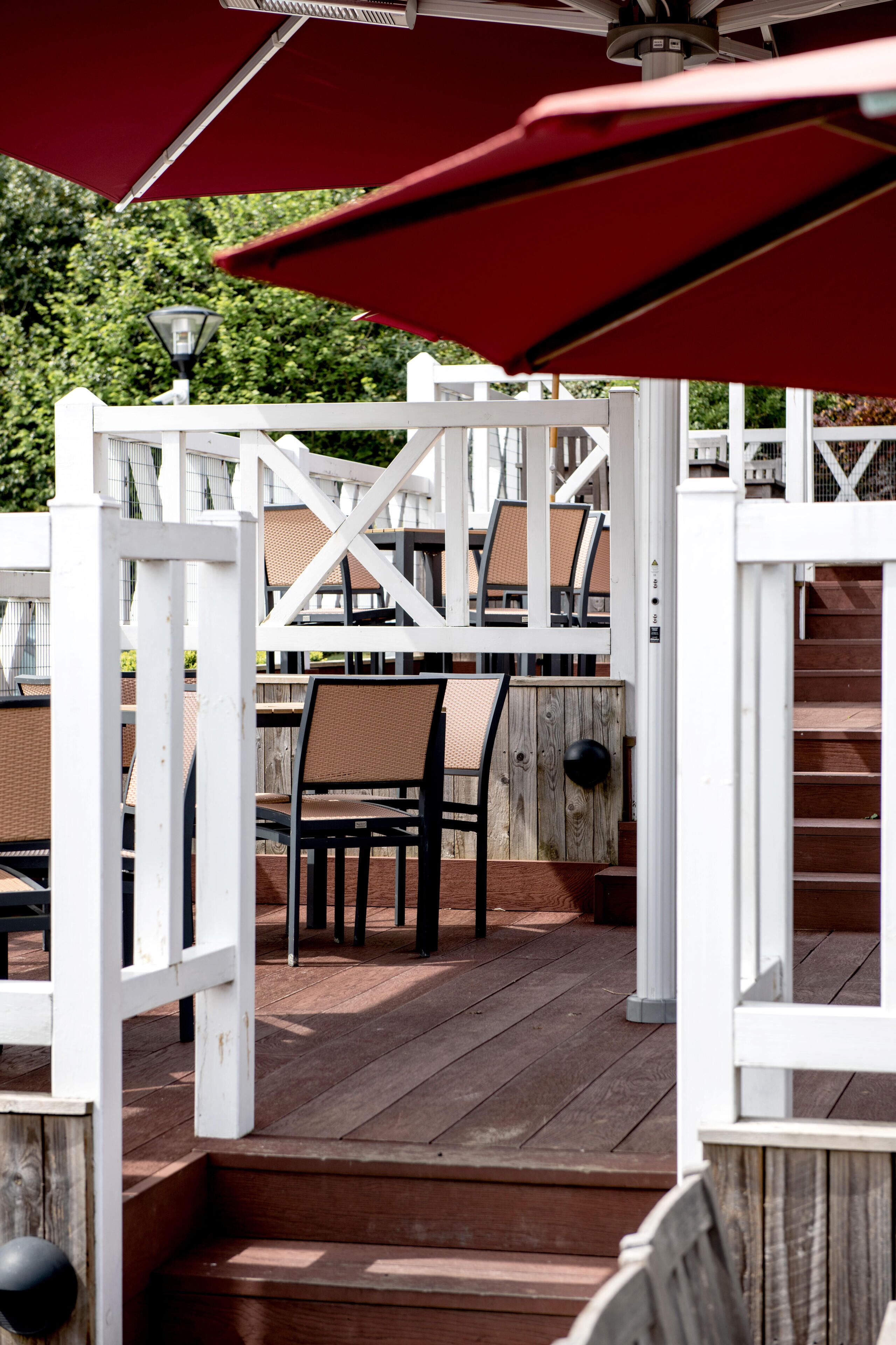 Une terrasse en bois avec des sièges d’extérieur, des rampes blanches et un parasol rouge.